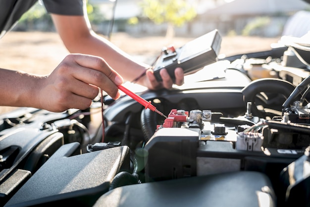 Mechanic repairman checking engine automotive in auto repair service and using digital multimeter testing battery to measure various values and analyze, Service and Maintenance car battery check.