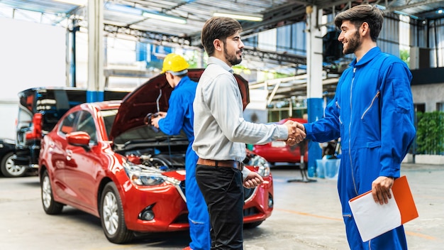 Il meccanico stringe la mano al cliente dopo aver finito di controllare l'auto rossa con il cofano aperto