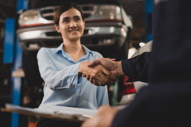 写真 ガレージで車のチェックを終えた後、顧客と握手するメカニック技術者の男性2人がプロの自動車修理サービスセンターで働く仕事のために握手する