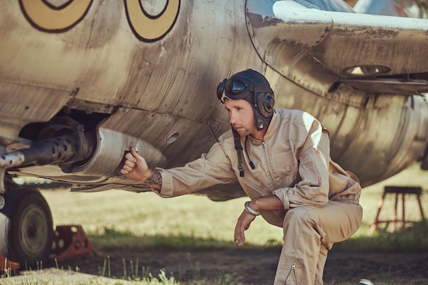 Mechanic in uniform and flying helmet repair old war fighter-interceptor in an open-air museum.