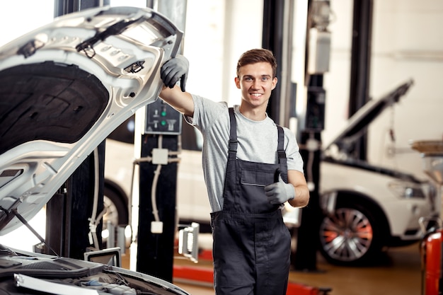 A mechanic in uniform is standing near a car.