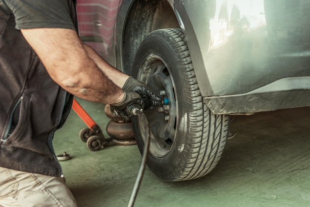 Механик с помощью электрической отвертки снимает колесо с автомобиля, который ремонтирует в гараже.
