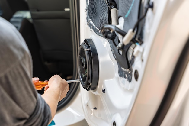 Mechanic using screwdriver screwing drywall screw with car speaker on vehicle door panel in garage