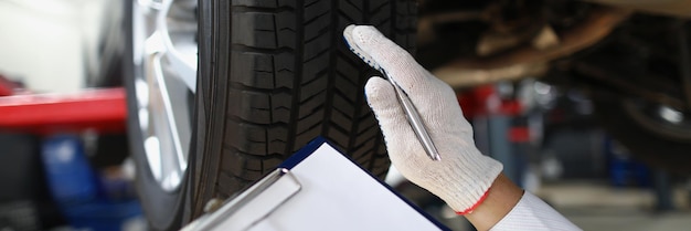 Mechanic worker point at tyre and write down in document notes