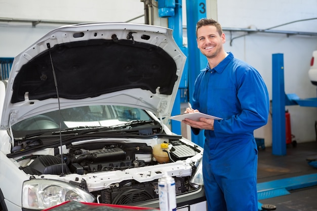 Mechanic writing on clipboard looking at camera