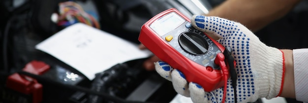 Foto mechanica houdt multimeterapparatuur in de hand om de spanning van de auto-accu te meten;