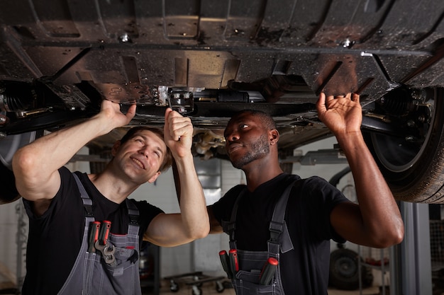 Mechanics checking car bottom in auto service