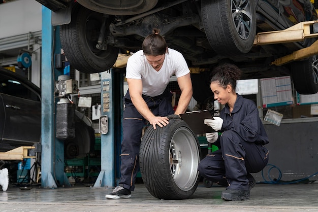 Механики мужчина и женщина проверяют и ремонтируют колесо автомобиля в гараже