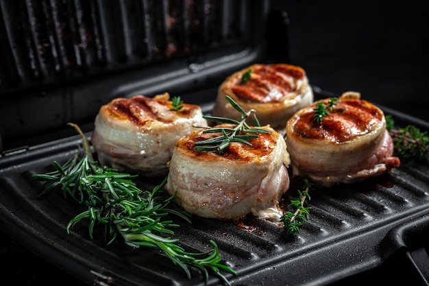 Photo medallions steaks from the beef tenderloin covered bacon on grill on dark background. top view.