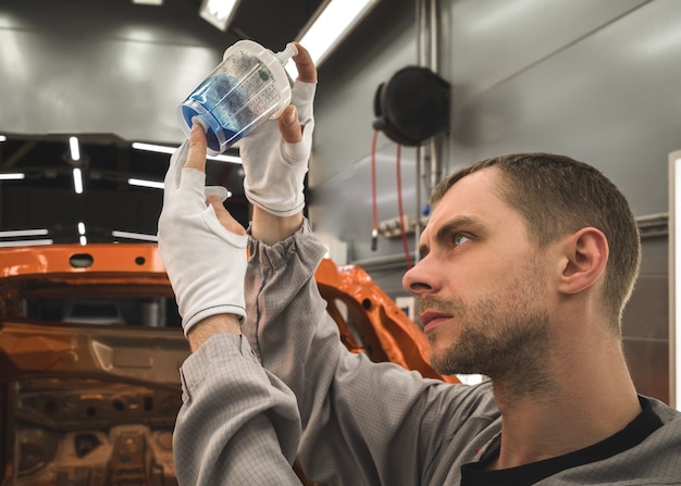 Medewerker van een autofabriek bereidt het basislak voor het lakken van auto's