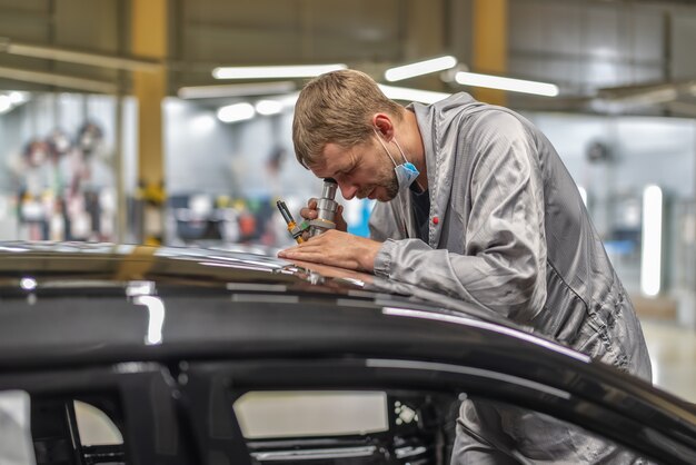 medewerker van een autofabriek controleert de kwaliteit van het schilderen met een microscoop