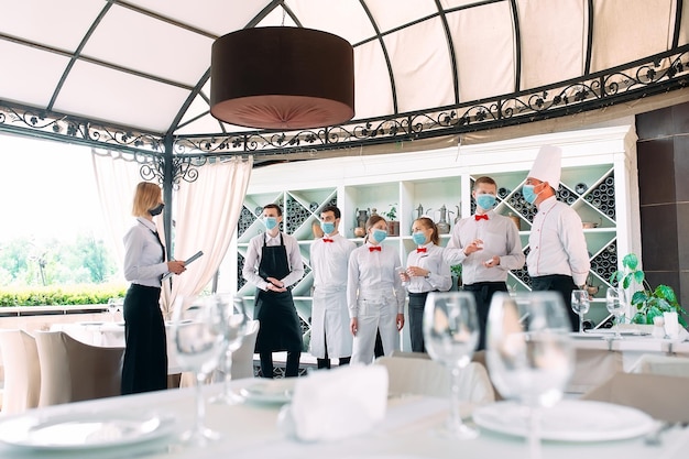 Medewerkers van een restaurant of hotel met beschermende maskers. Einde quarantaine. Restaurantmanager en zijn personeel op het terras. interactie met de chef-kok in het restaurant.