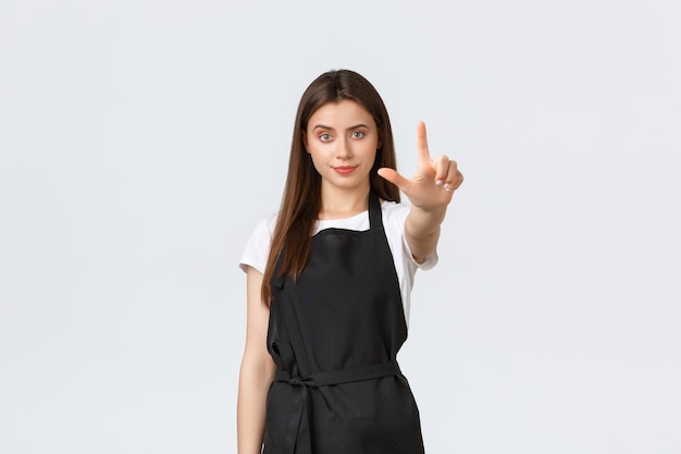 Medewerkers van supermarkten, kleine bedrijven en coffeeshops concept. Ernstige jonge vrouwelijke cafémedewerker in zwarte schort met uitgestrekte vinger in verbod, beperk of waarschuw gasten.