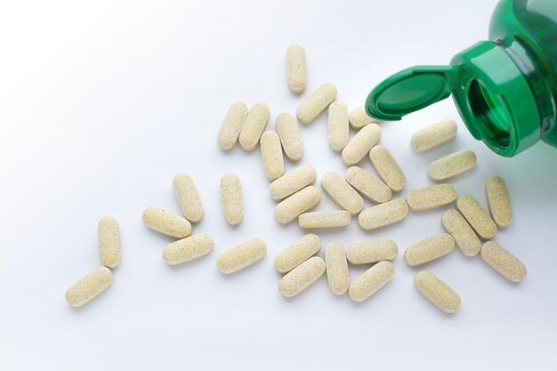 Medial pills are scattered from green bottle on white table.