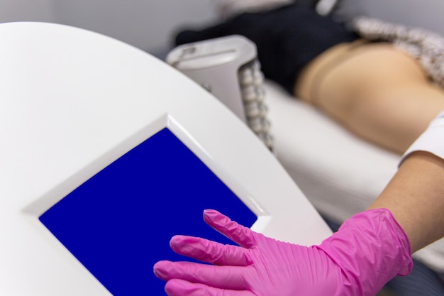 Медик регулирует режим работы антицеллюлитного массажного аппарата с технологией сжатия и вибрации в кабинете косметолога