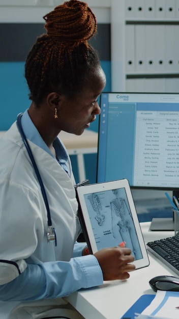 Medic explaining osteopathy diagnosis on tablet to ill patient in doctors office. Doctor and woman analyzing human skeleton image on device for osteoporosis treatment and healthcare