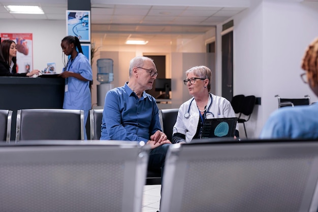 Medico e paziente anziano che esaminano la scansione cerebrale sul laptop, analizzando il sistema neurale sulla tomografia nella hall della struttura. medico che spiega la diagnosi neurologica sul computer all'uomo anziano in sala d'attesa.