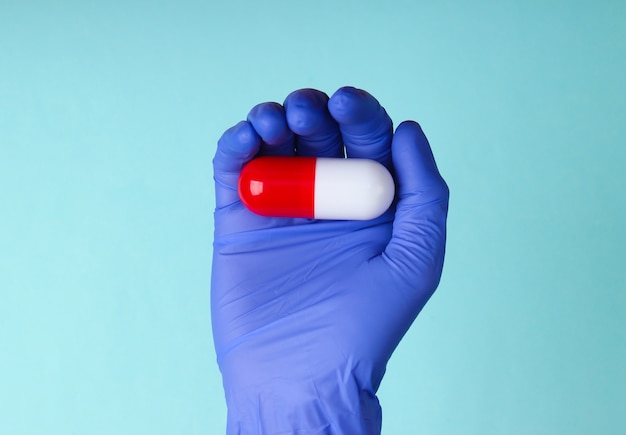 Medic's hand in latex gloves holds capsule on blue background. Medical concept