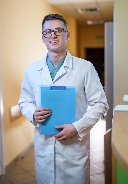 Medic in scrubs holds folder and stands in clinic corridor ready to give consultation. Hospital and healthcare concept.