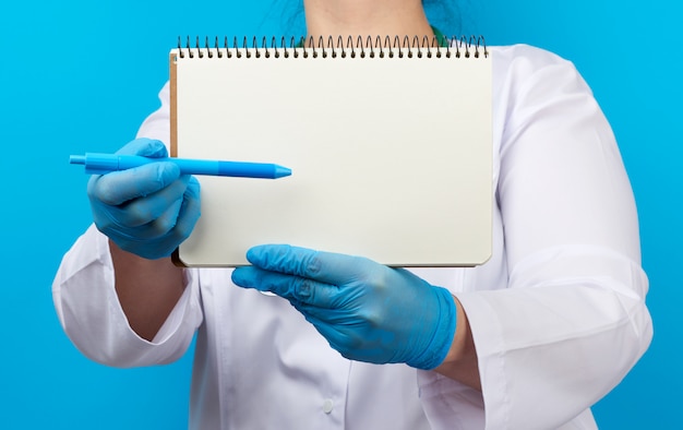 Medic vrouw in witte jas, blauwe latex handschoenen met een open notitieblok met lege witte lakens