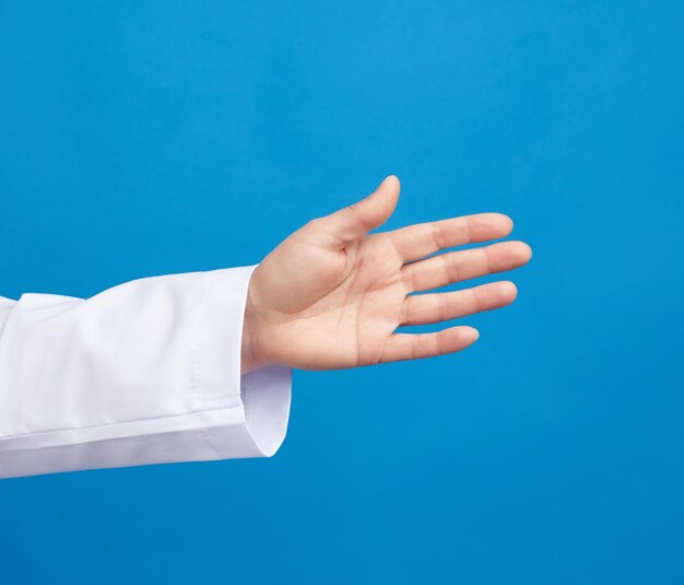 Medic in a white coat pulls his hand for a handshake on a blue background close up