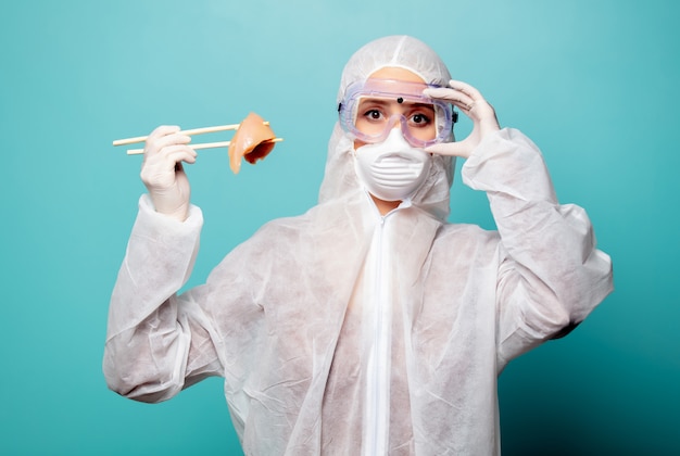 Foto la donna dell'erba medica che indossa l'abbigliamento protettivo contro il virus tiene la carne cruda con le bacchette cinesi