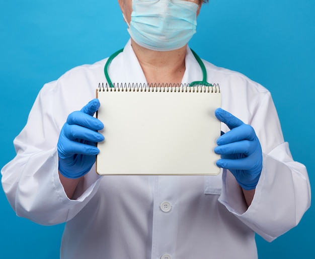 Medic woman in white coat, blue latex gloves holding an open notebook with white sheets