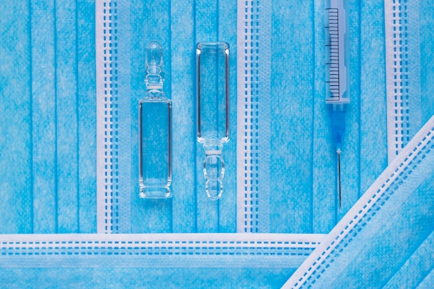 Medical ampoules and syringe on the blue masks background Vaccina and vaccination concept