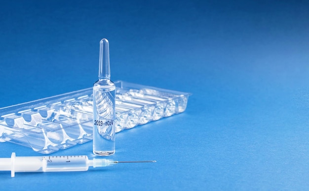 Medical ampoules and syringe with injection isolated on blue background with copy space coronavirus vaccine to stop the virus