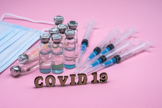 マスクとシリンジをピンクの背景に COVID-19 ワクチン接種