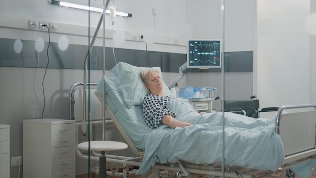 Medical assistant looking at heart rate monitor while patient
sleeping in hospital ward bed. nurse checking up on retired woman
with nasal oxygen tube for healthcare and recovery.