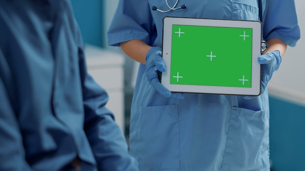 患者と相談してデジタルタブレットの緑色の画面を使用する医療助手。クロマキーテンプレートと分離されたコピースペース、空白のモックアップの背景を持つデバイスを保持している女性。