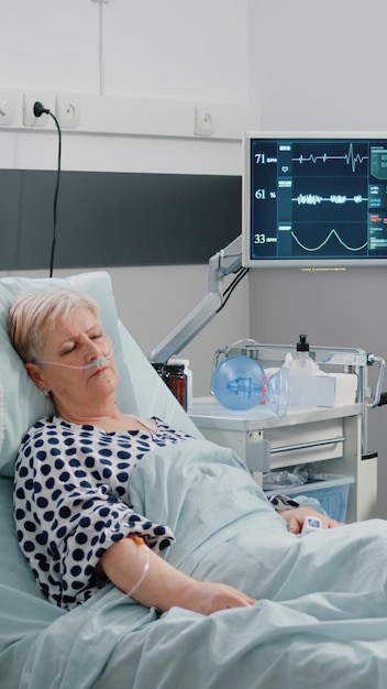 병원 병동 침대에서 자고 있는 은퇴한 환자를 방문하는 의료 보조. 맥박 측정을 위해 심박수 모니터를 확인하는 간호사로 일하는 여성. 사람을 돌보는 전문가
