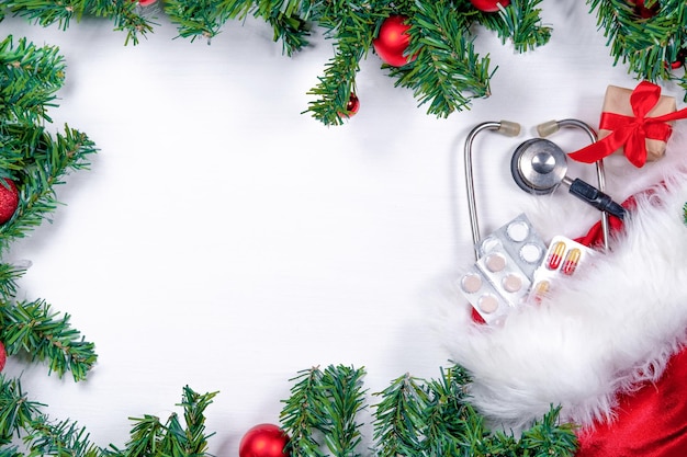 Insegna medica con lo stetoscopio della scatola del regalo delle pillole e l'albero di natale su fondo di legno bianco