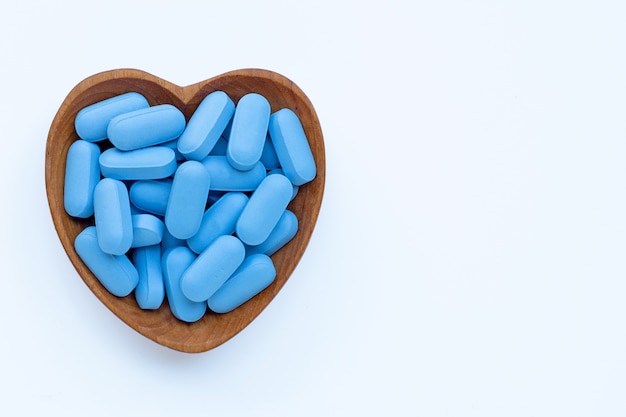 Medical blue pills with heart shaped wooden bowl on white background.