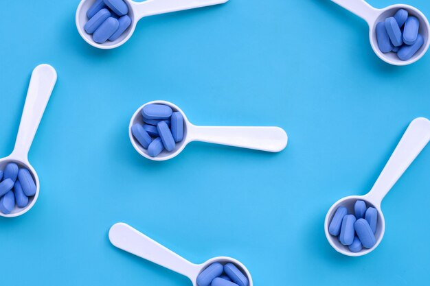 Medical blue pills with white plastic spoon on blue background.