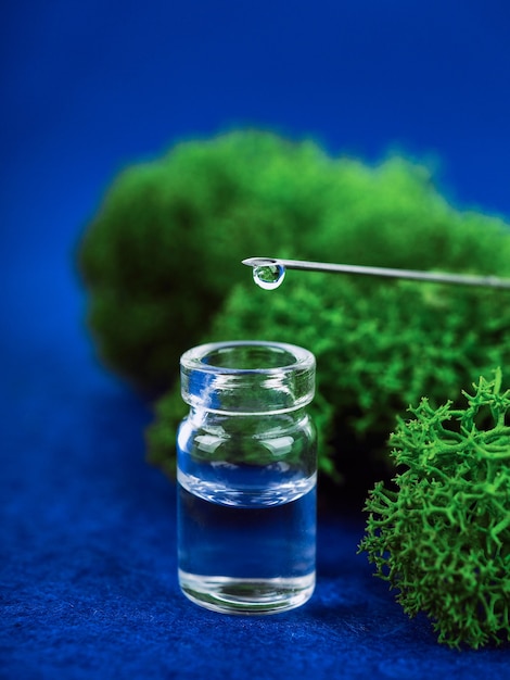 Medical bottle, drop on a needle in the background moss