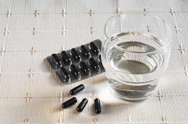 Photo medical capsules with activated charcoal and glass of water on tablecloth