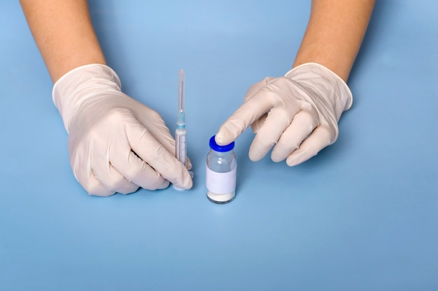 Medical concept. On a blue background doctor's hands in white gloves, coronavirus vaccine, syringe. virus protection.Concept: prevention of coronavirus