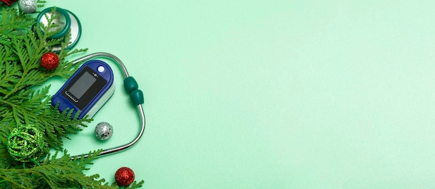 Medical concept: celebrating Christmas in healthcare. Top view of a flat lay close-up of a stethoscope, pulse oximeter with fir branches on a green background. copy space