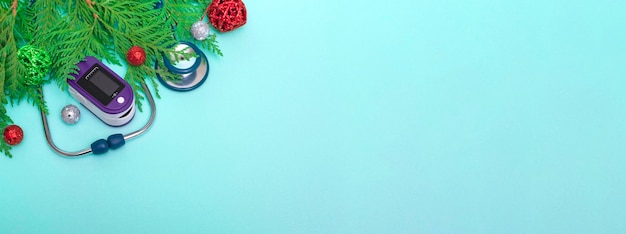 Medical concept: celebrating Christmas in healthcare. Top view of a flat lay close-up of a stethoscope, pulse oximeter with fir branches on a green background, copy space.