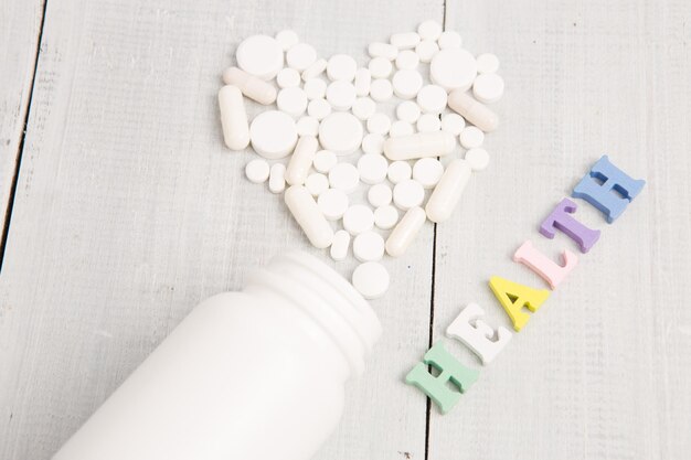 Medical concept color HEALTH inscription and white heart of pills and capsules on white wooden desk