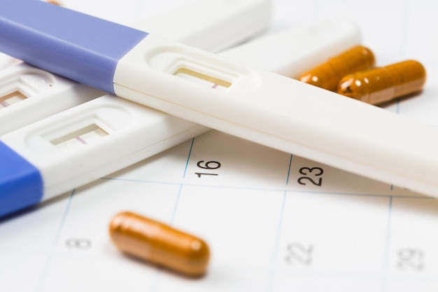 Photo medical concept, pregnancy tester on calendar and pills close up.