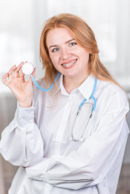 Medical concept Smiling nurse with braces and a stethoscope in her hand Happy and laughing female doctor in a white coat posing at the camera Hospital worker