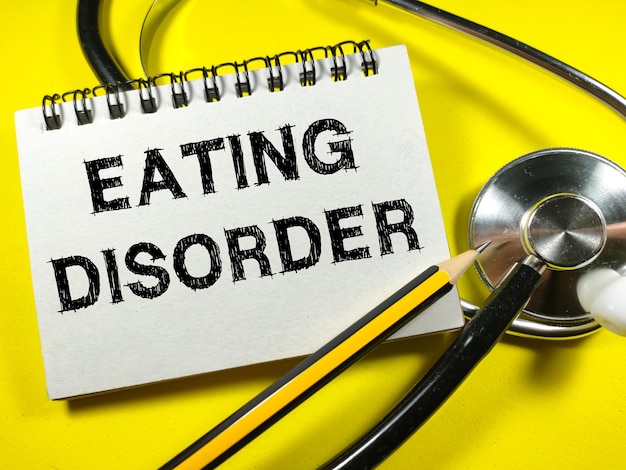 Medical concept Text EATING DISORDER on notebook with stethoscope and pencil on yellow background