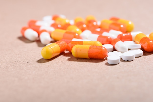 Медицинская концепция: белые, оранжевые таблетки и капсулы на коричневом фоне.