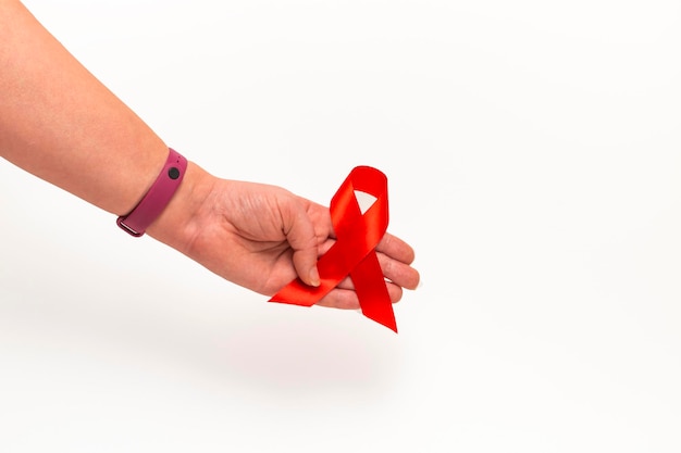 Concetto medico per la giornata mondiale contro l'aids a dicembre. nastro rosso di sensibilizzazione sull'aids stretto nella mano di una donna su uno sfondo bianco. avvicinamento