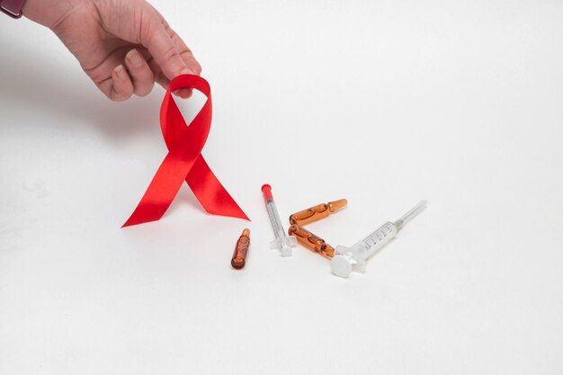 Medical concept for world aids day in december. red aids\
awareness ribbon clutched in a woman\'s hand on a white background.\
close up