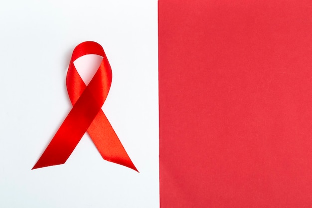 Medical concept for World AIDS Day in December. Red AIDS awareness ribbon on white and red background. Close up copy space