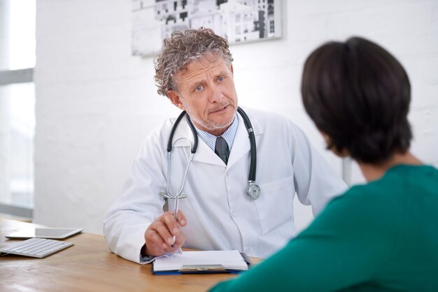 Medical consultation and mature doctor with a checklist for healthcare insurance or results of test Clinic patient and man in discussion of surgery or exam and professional paperwork for hospital